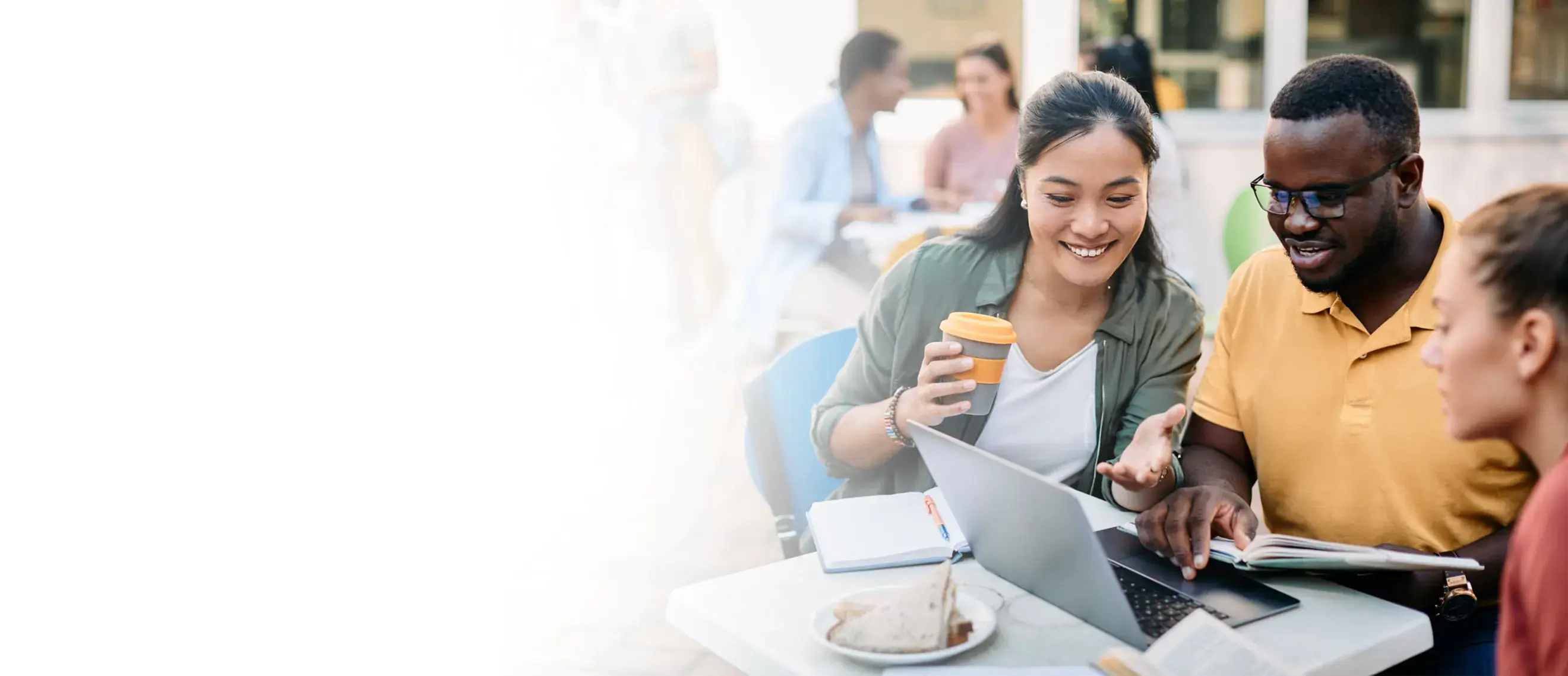 Three people in a university courtyard setting working on a laptop and drinking coffee